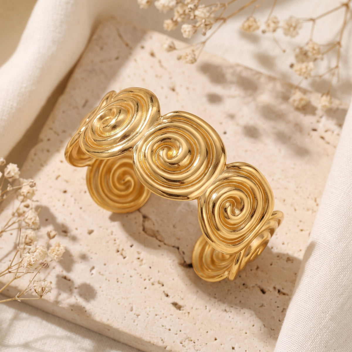 Angled overhead view of the gold-tone spiral cuff bracelet resting on a beige textured stone surface.