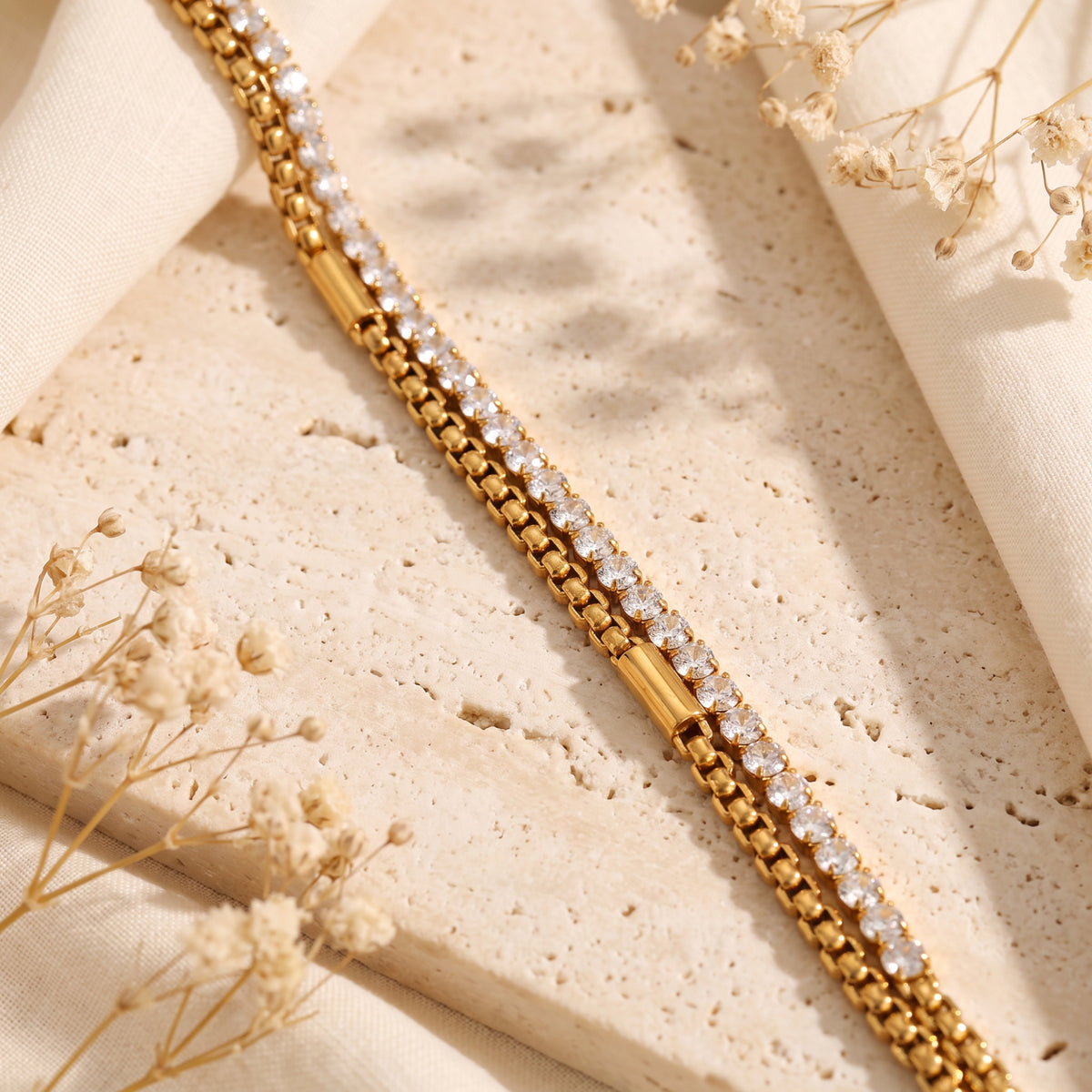 Close-up view of the gold-tone double-layer bracelet laying diagonally on a beige stone tile.