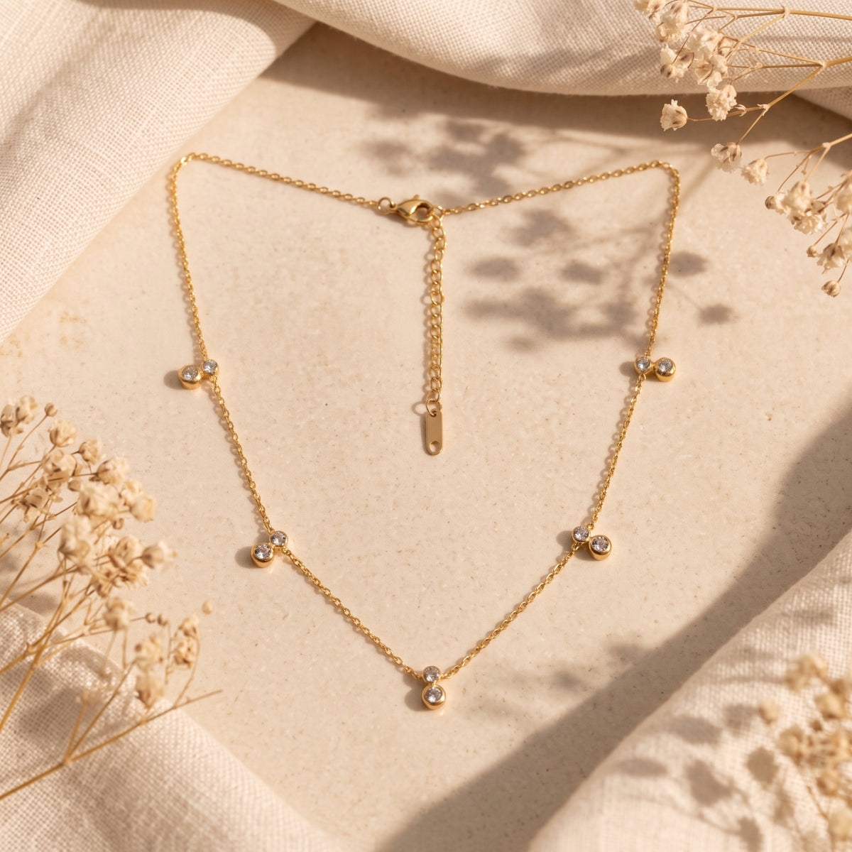 Full layout of the gold-tone bezel station necklace with five stations, clasp, and extender chain visible.