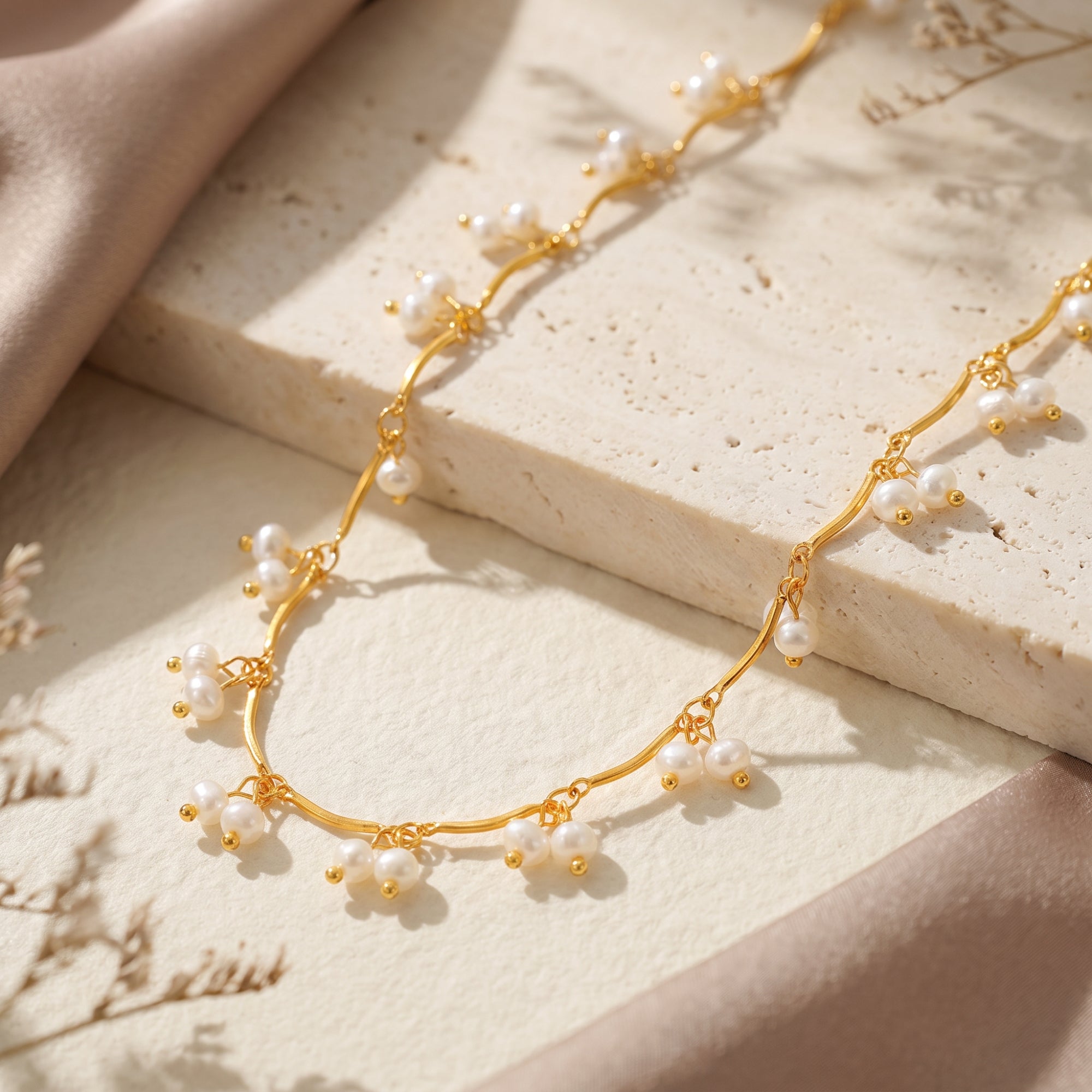 Macro detail of the wavy gold chain and white drop pearls on the Aurendra stainless steel necklace.