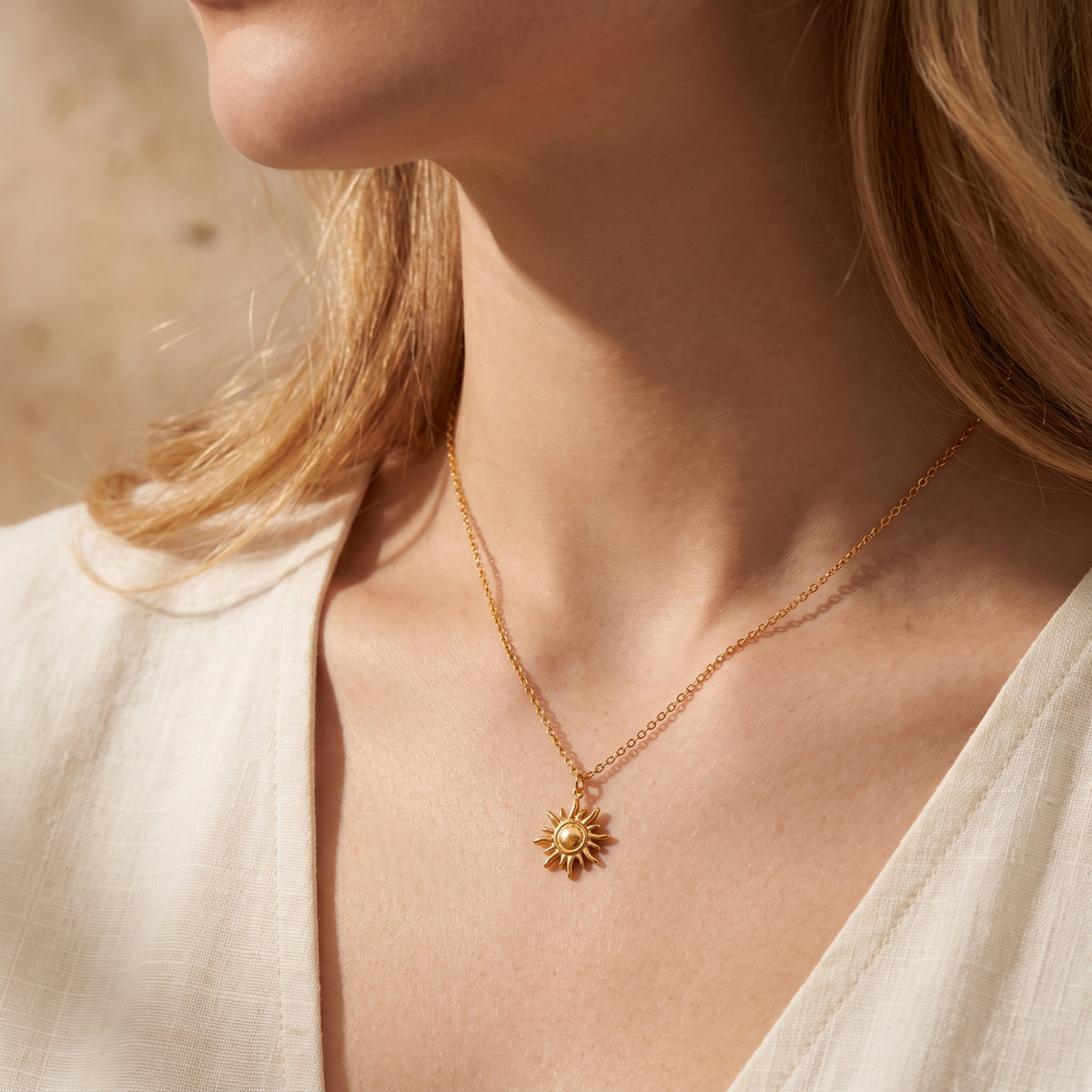 Close-up of a woman wearing the gold-tone sun pendant necklace with a white V-neck top.