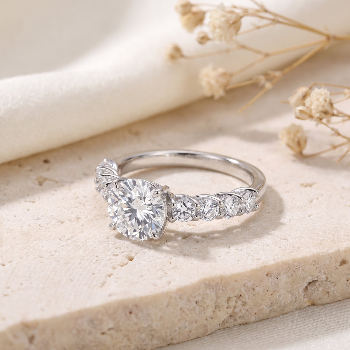 Silver ring with a large round center stone and accent stones resting on a light-colored stone block.