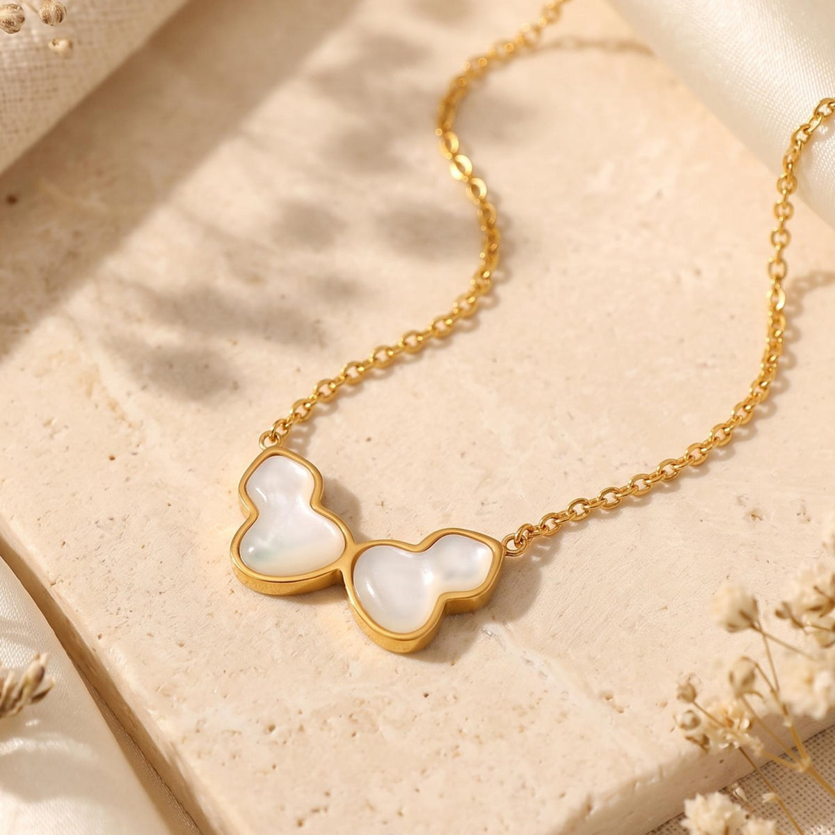 Angled view of a gold-tone chain necklace with a white iridescent butterfly pendant on a stone surface.