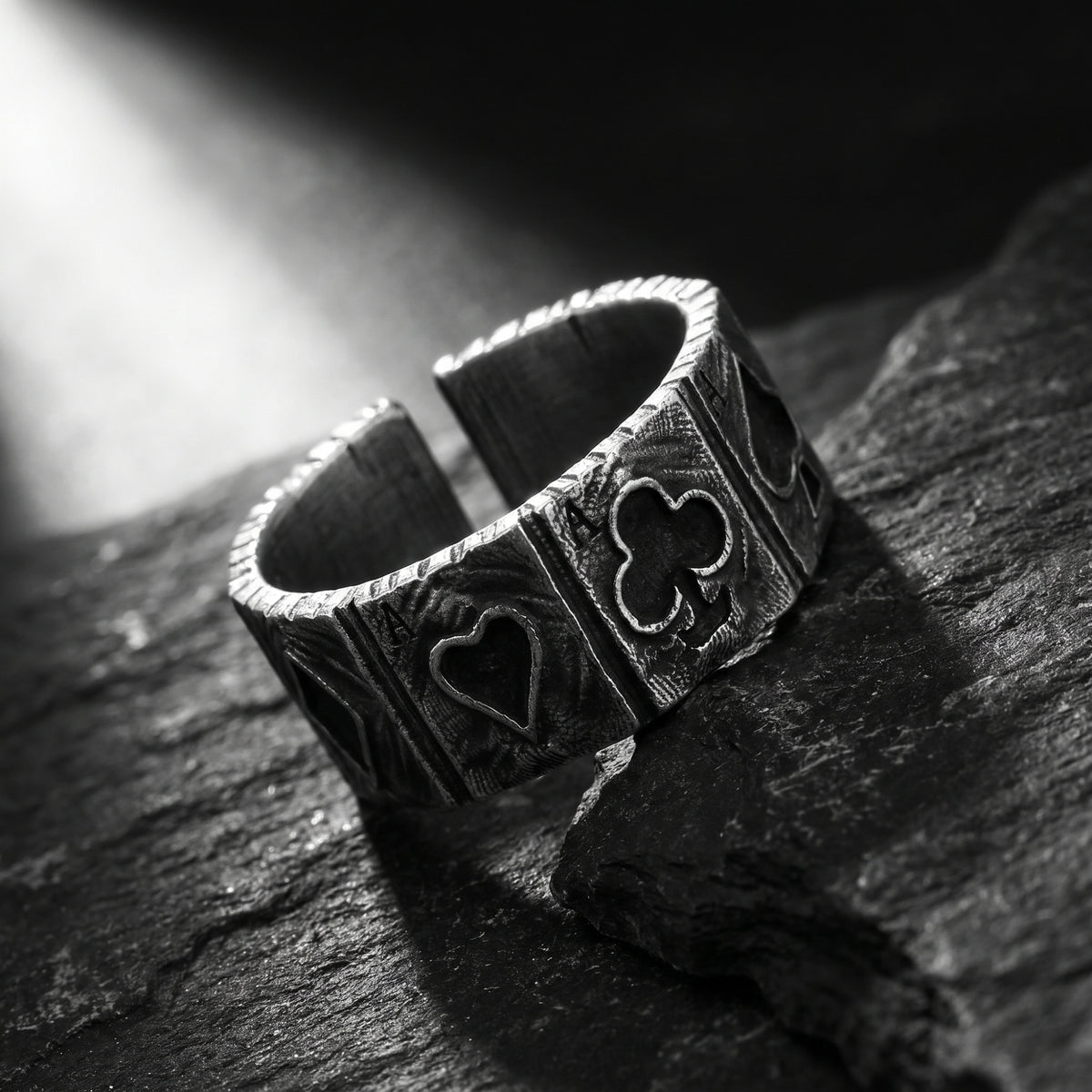 Angled view of the silver open band ring on slate, showing its open back and card-suit motifs.