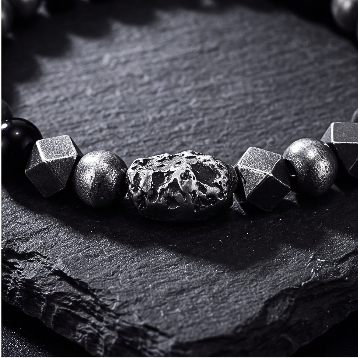 Extreme close-up of the textured silver centerpiece bead and geometric polyhedral accents on dark slate.