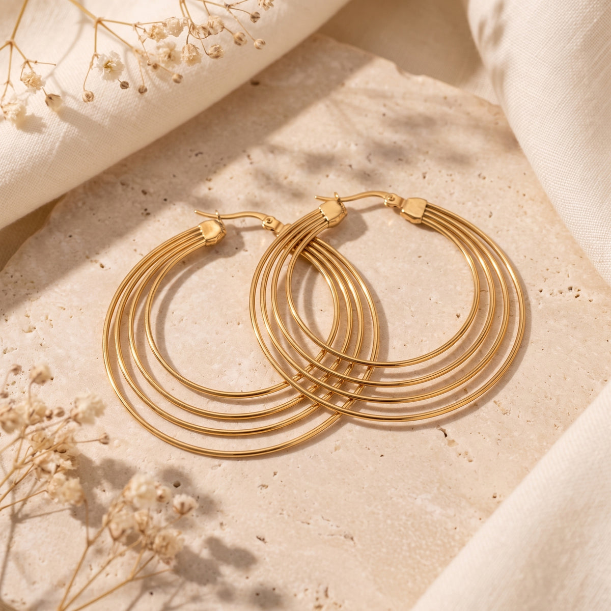 Overhead flat lay of two gold-tone four-ring hoop earrings crossed on a textured stone block.