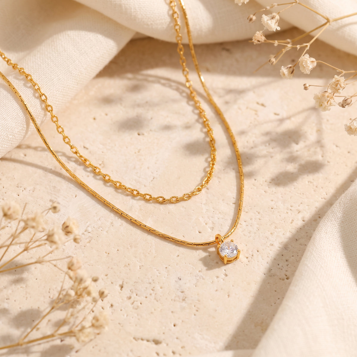 Flat lay of the gold-tone double-strand necklace with a round pendant on textured stone.