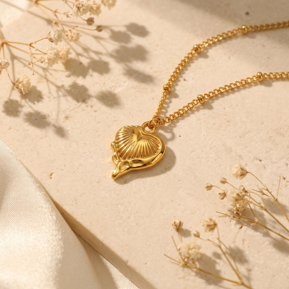 Flat lay view of the gold-tone fluted heart pendant necklace displayed on a textured stone surface.