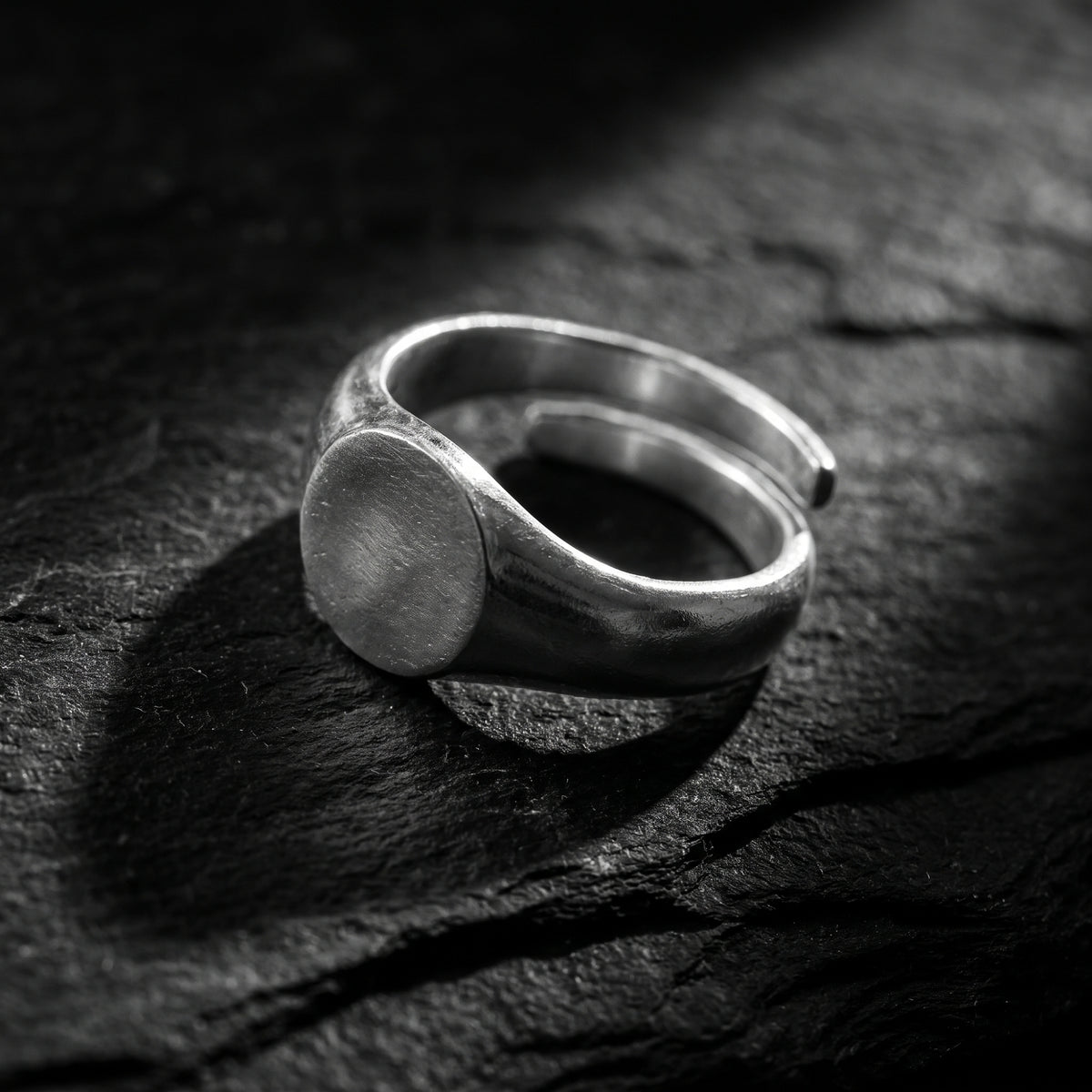 Angled view of the silver open-band ring on dark textured stone, showing its circular face and visible gap.