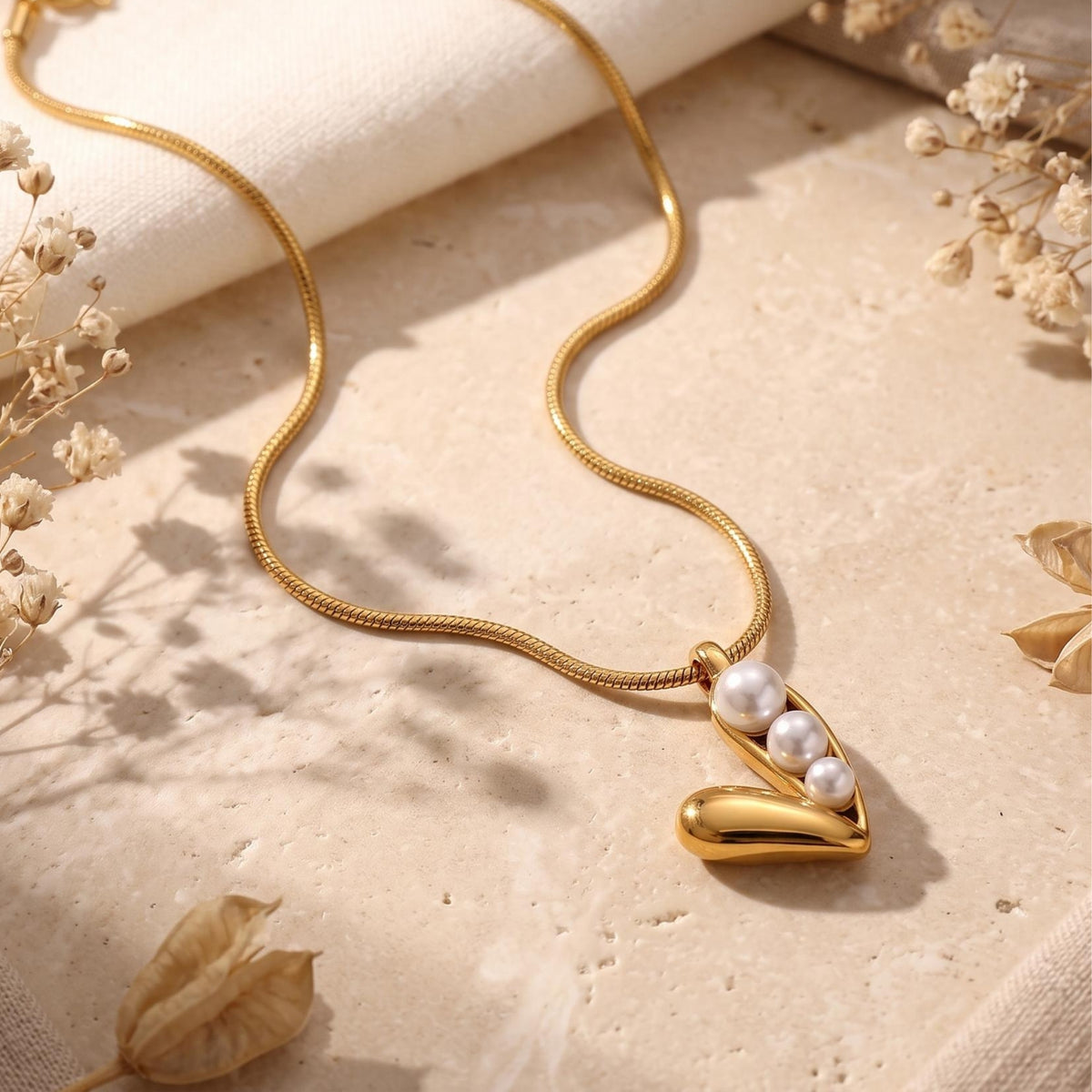Flat lay of the gold-tone pod necklace with three white simulated pearls on textured beige stone.