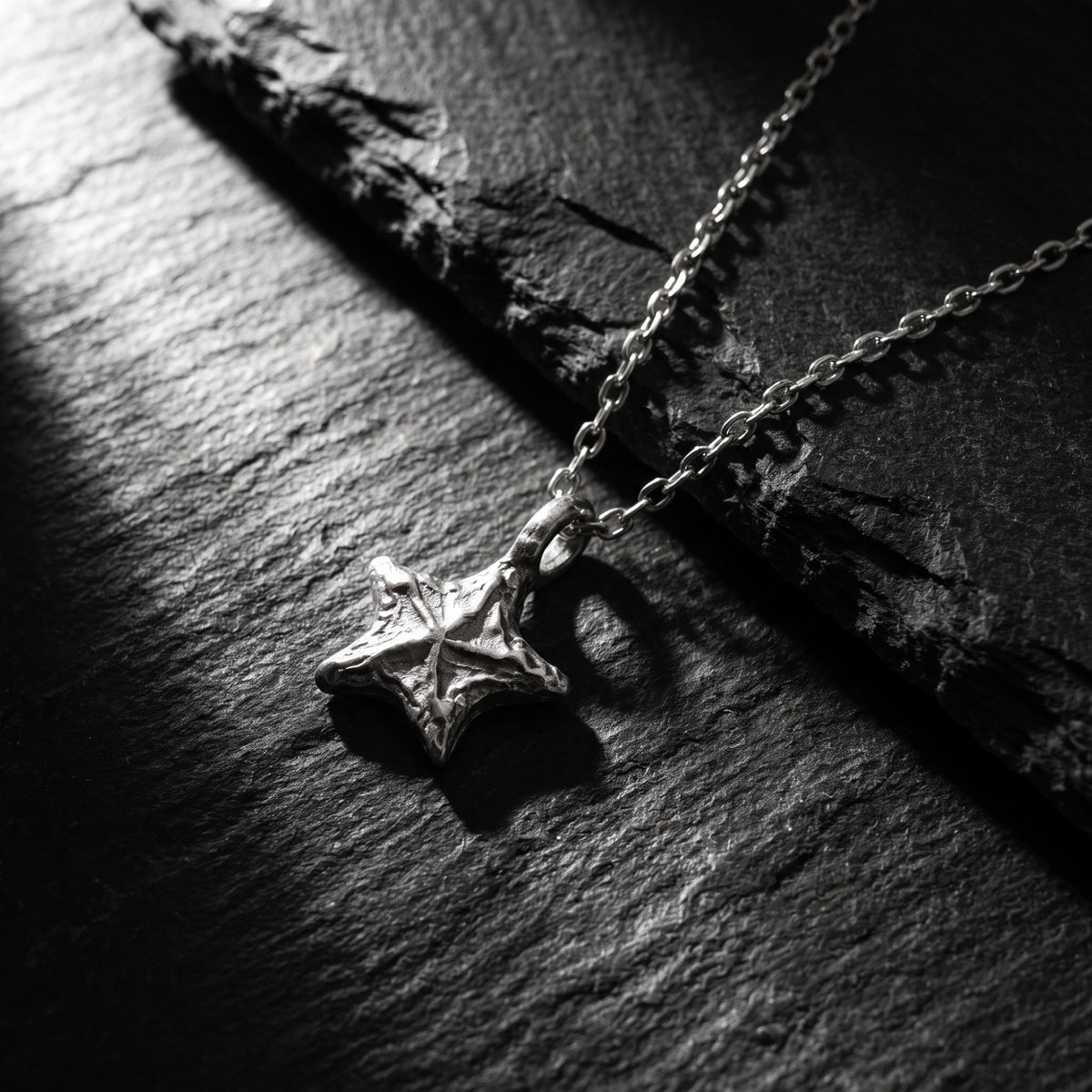 Angled close-up of the textured silver starburst pendant and chain resting on a dark stone surface.