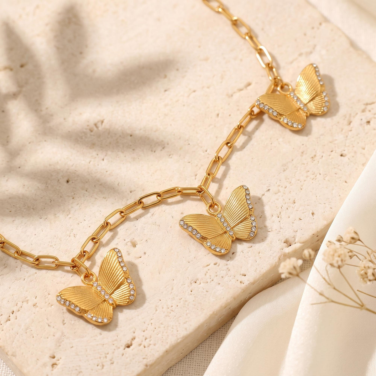 Close-up view of three gold-tone textured butterfly charms with clear stone borders on paperclip chain.