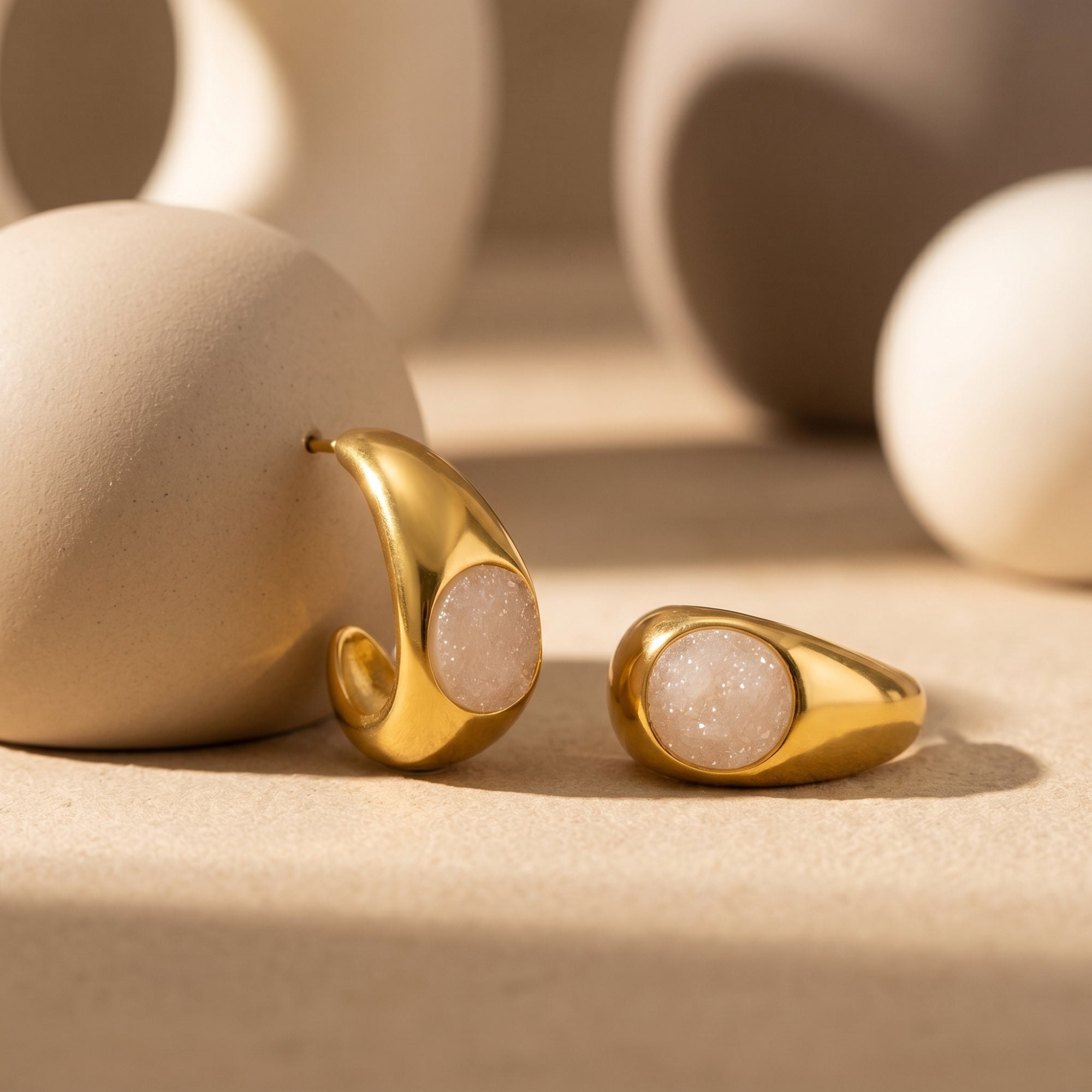 Gold PVD teardrop earring and quartz jewelry on neutral background.
