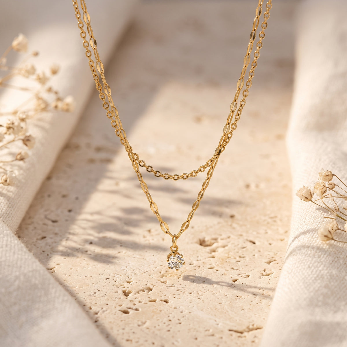 The layered gold-tone necklace hanging suspended, showcasing the round clear stone pendant centered.