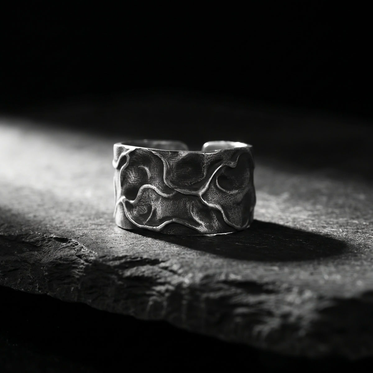 Front view of the wide silver open band ring resting on dark stone under focused lighting.