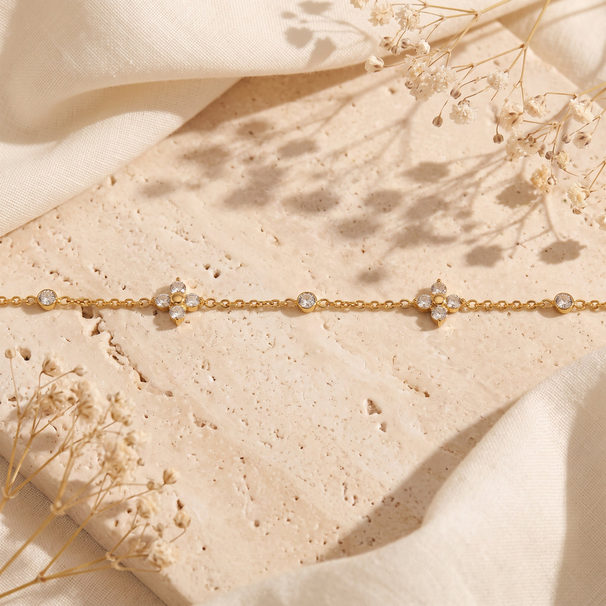 Flat-lay view of the gold-tone bracelet showing cubic zirconia clover motifs and round bezel stations on stone.
