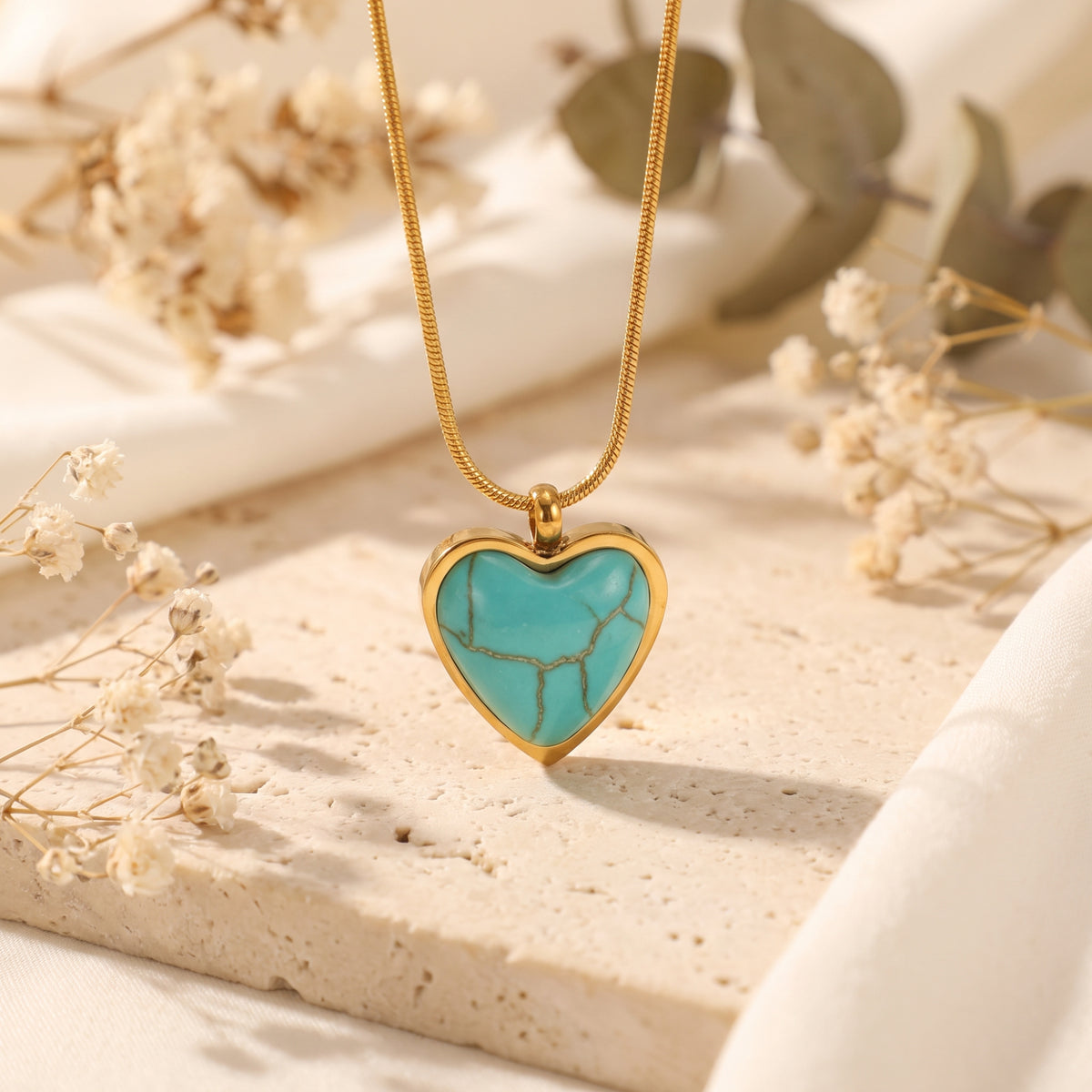Upright heart-shaped turquoise pendant in a gold-tone bezel, displayed on a beige stone slab.