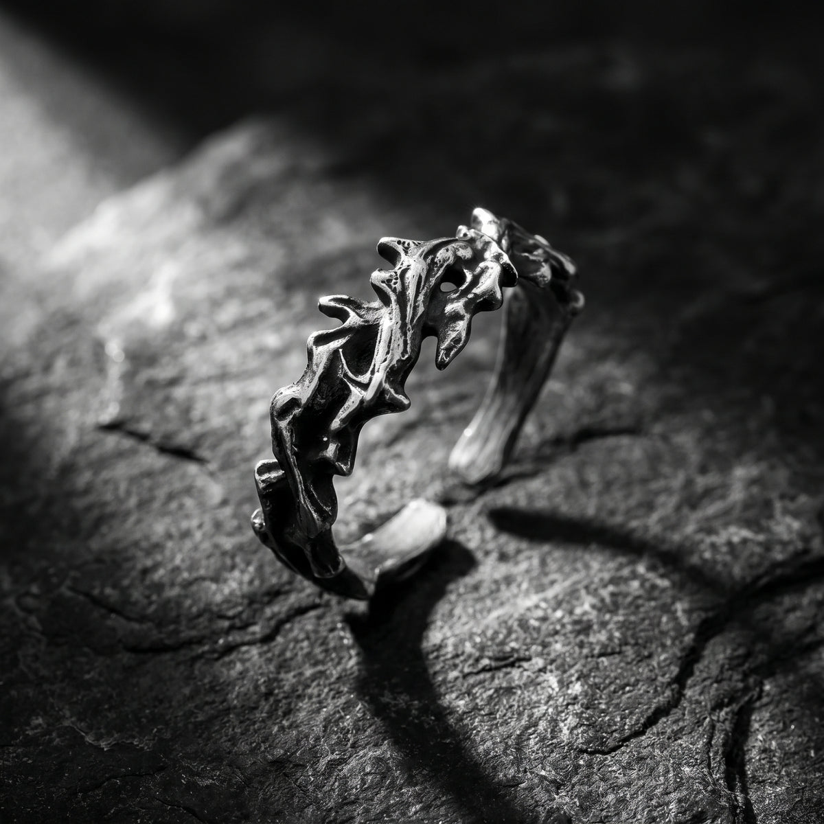 Angled view of the oxidized silver thorn open band ring on dark stone, showing its open gap.