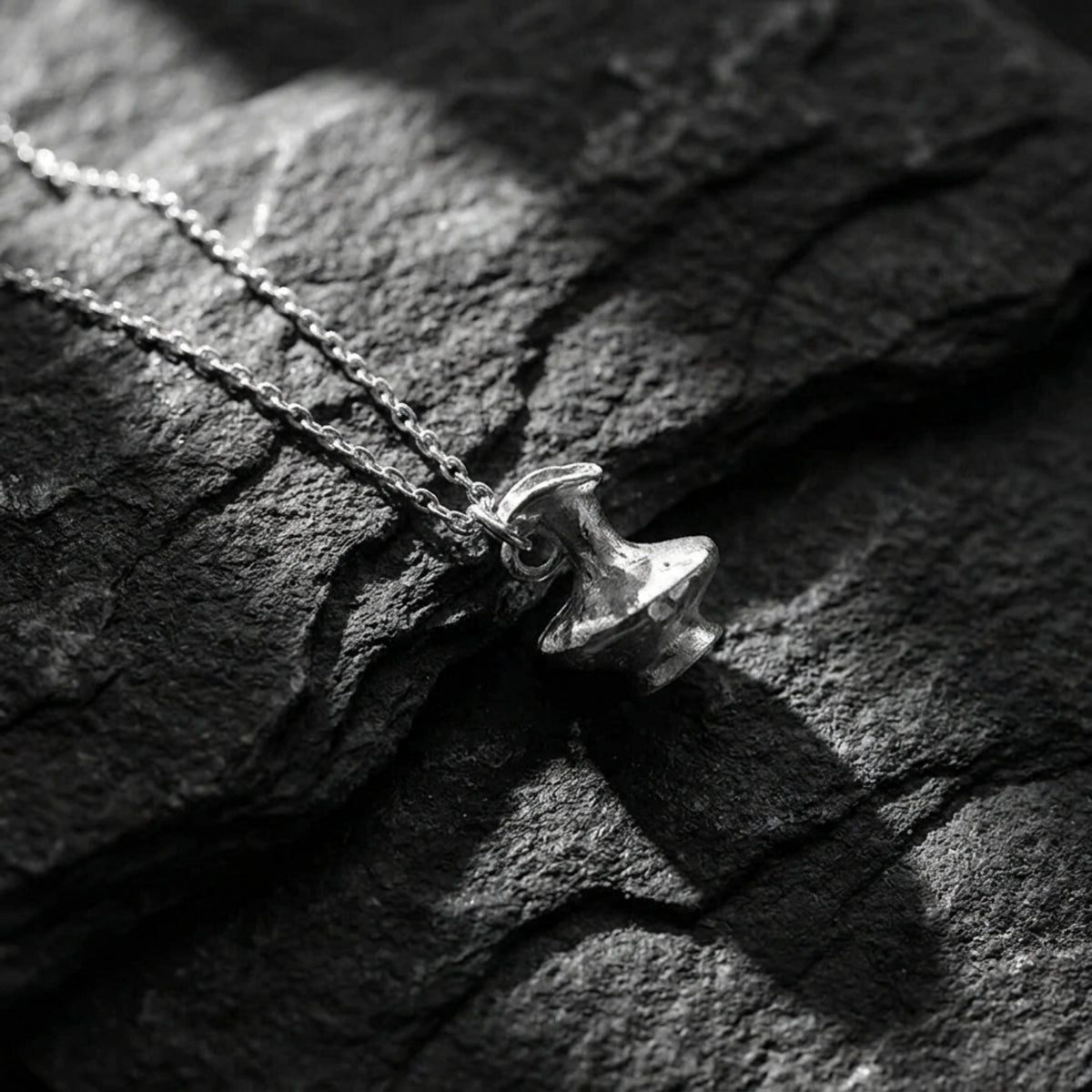 Silver vessel pendant and chain lying diagonally on dark, textured slate.