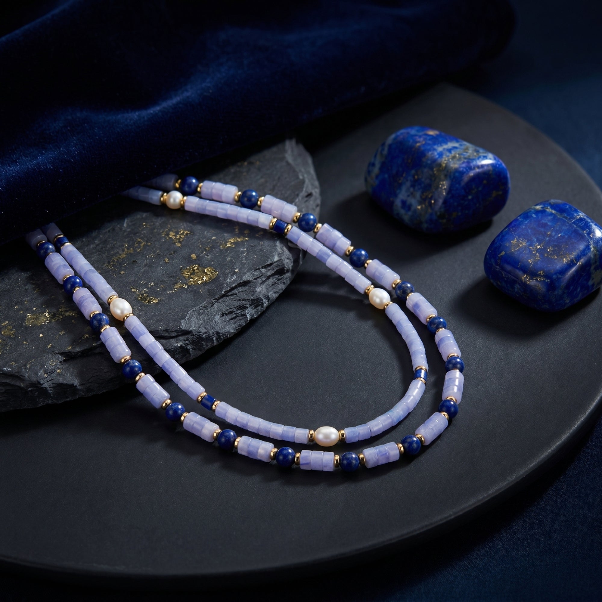 Close-up of gold plated layered necklace with cylindrical light blue beads, round lapis, and irregular pearls.