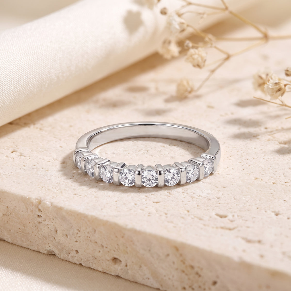 Front view of a silver ring resting flat, showing round clear stones in a bar setting.