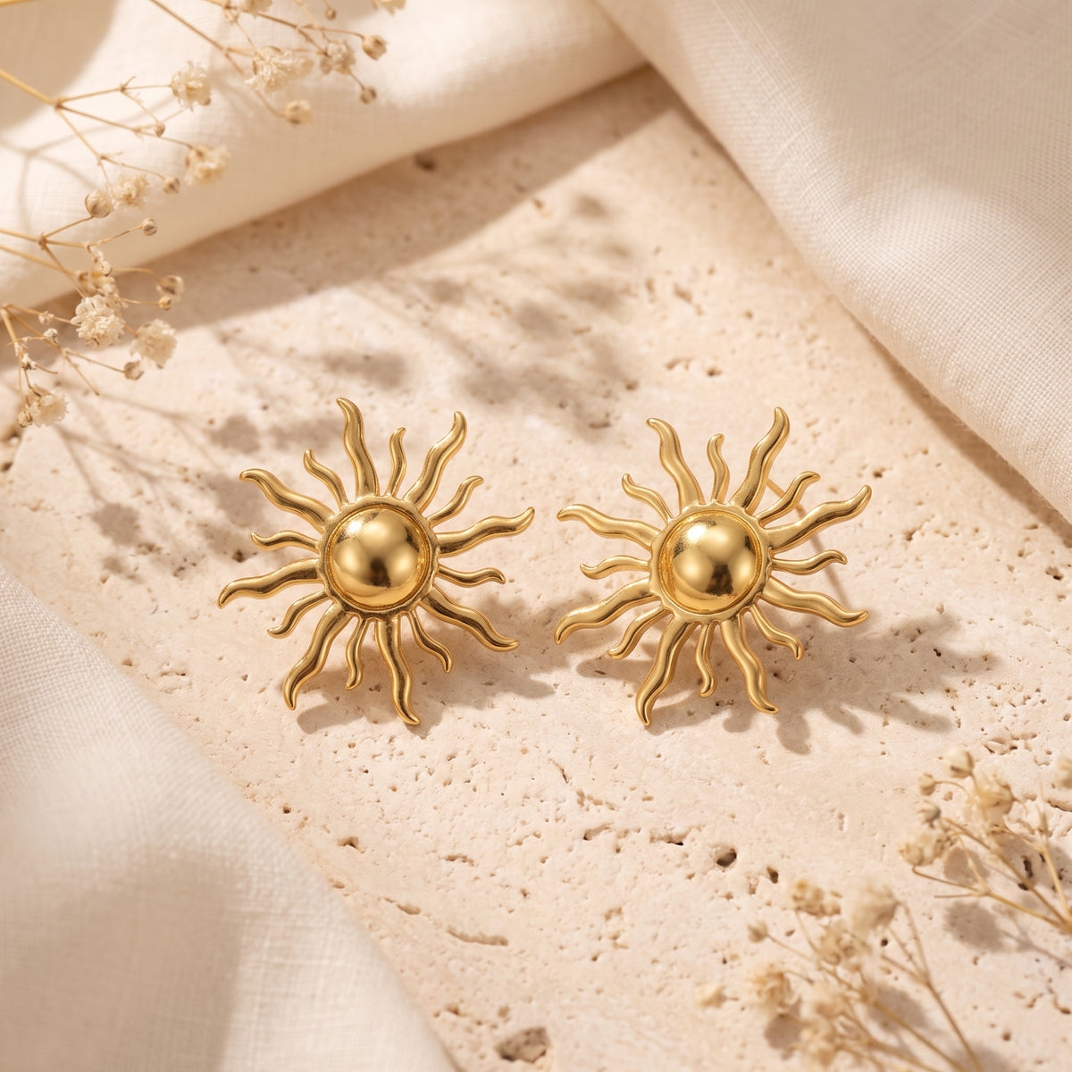 Pair of gold-tone sunburst stud earrings placed side by side on a light stone surface.