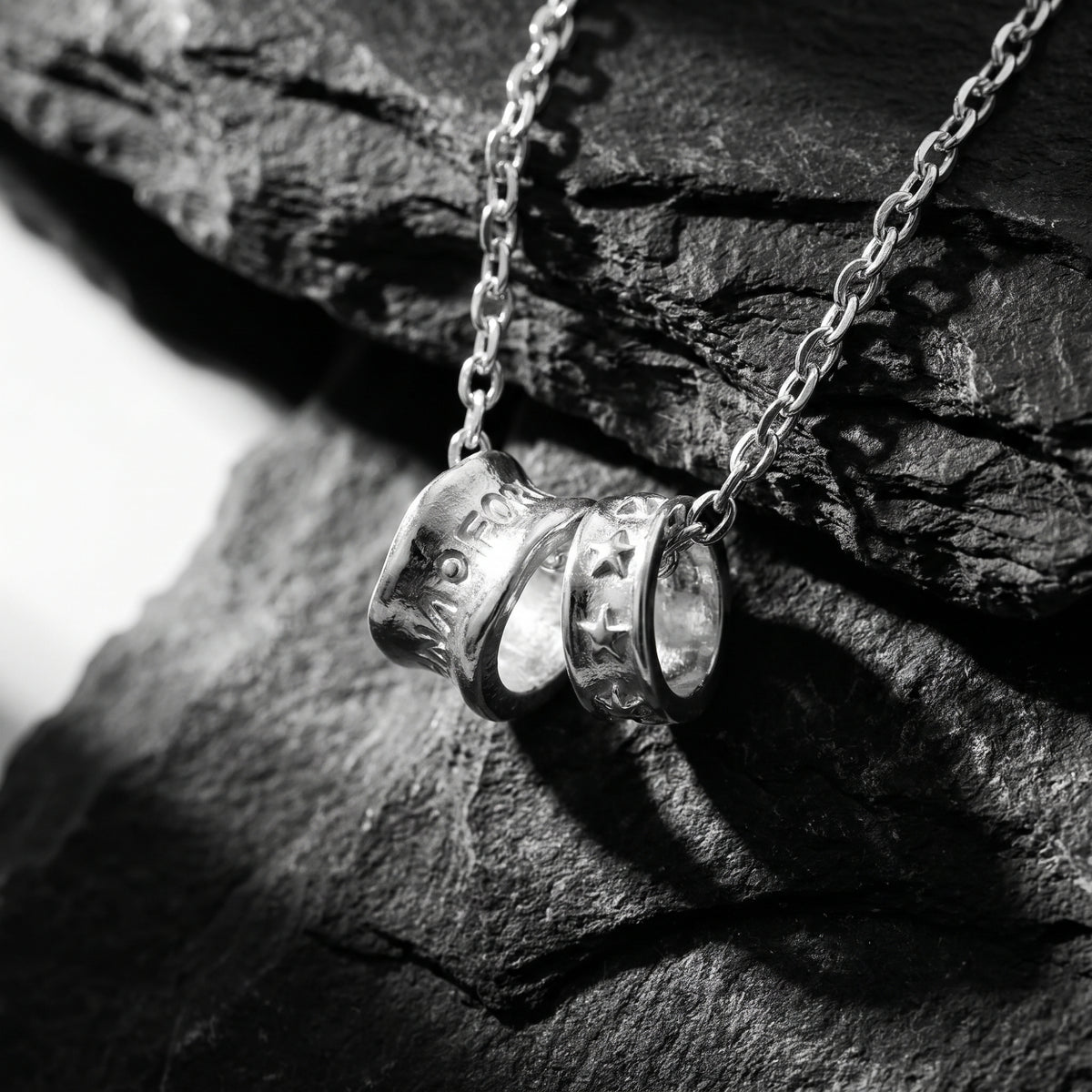 Close-up of twin silver cylinder pendants with engraved stars and lettering on dark slate.