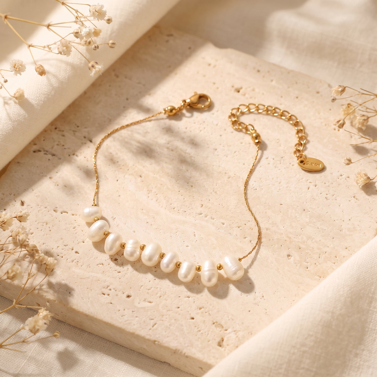 Unclasped gold-tone pearl station bracelet arranged open on a porous stone slab, with clasp and extender chain visible.