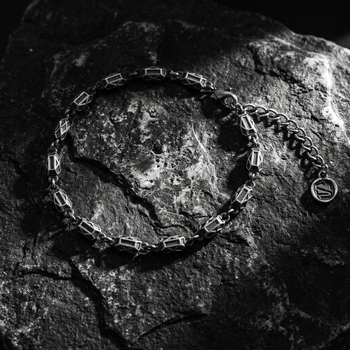 Overhead view of the silver geometric link bracelet on textured rock, showing its round logo charm.