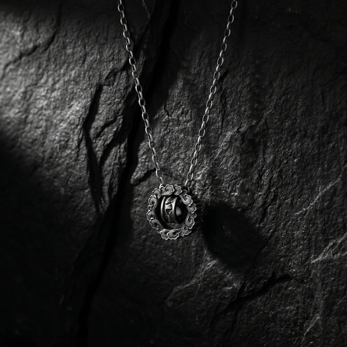 Silver cloud wheel pendant hanging against a textured black slate surface.