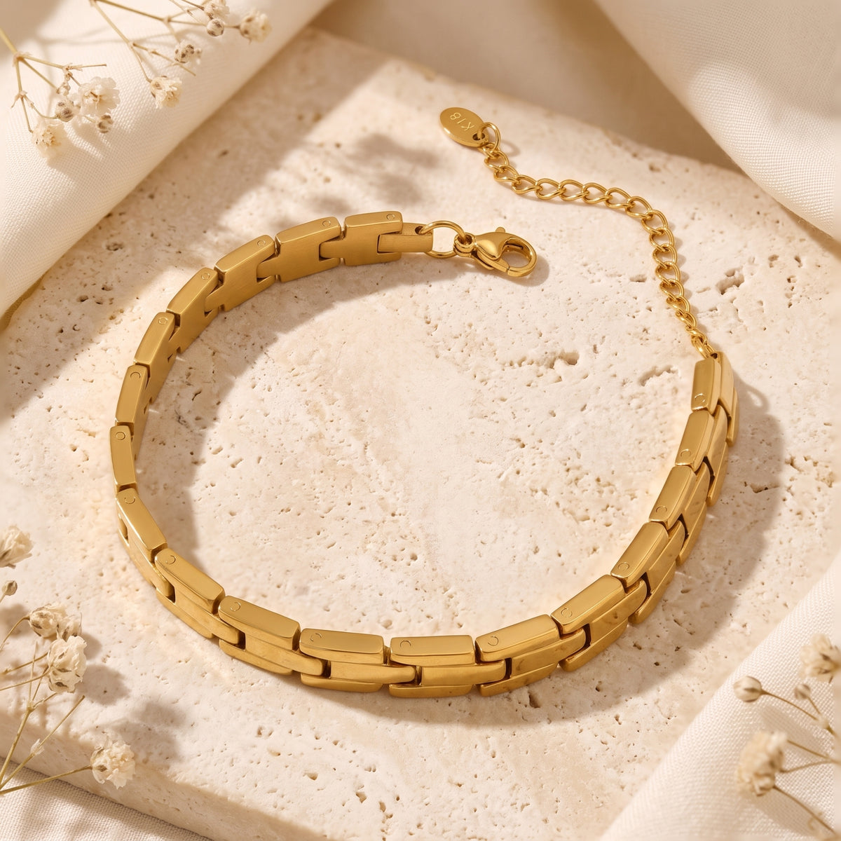 Overhead view of the gold-tone link bracelet arranged on stone with its lobster clasp and extender chain.