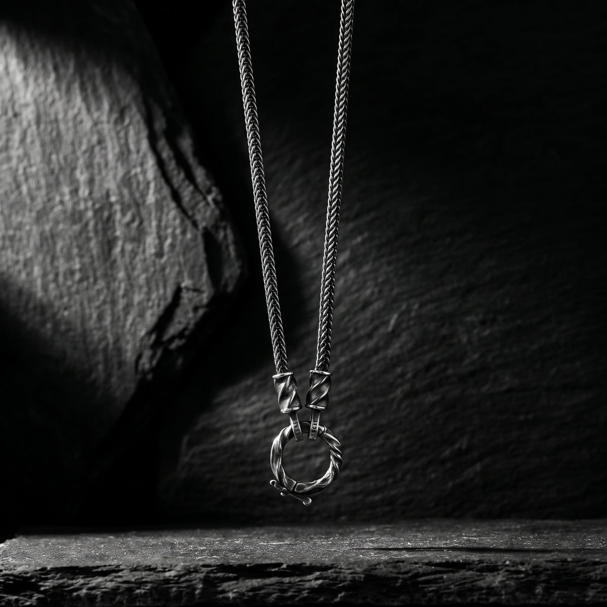 Silver twisted ring necklace suspended vertically against a dark slate background.