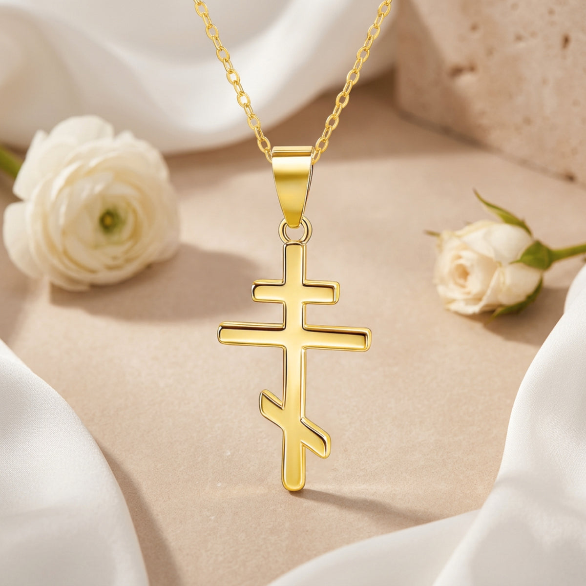 Front view of a gold-tone Eastern cross pendant necklace displayed between white roses.
