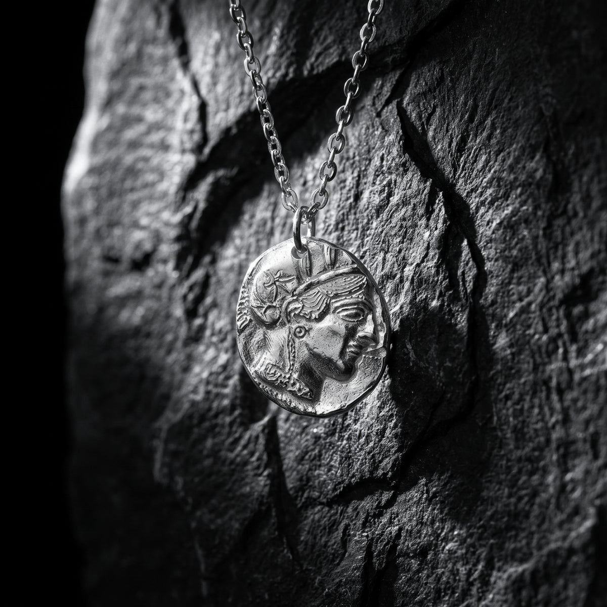 Silver Athenian coin pendant hanging vertically against a textured dark slate background.