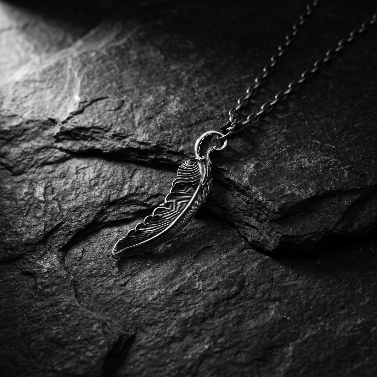 Close view of the silver feather pendant and chain lying on dark textured stone.