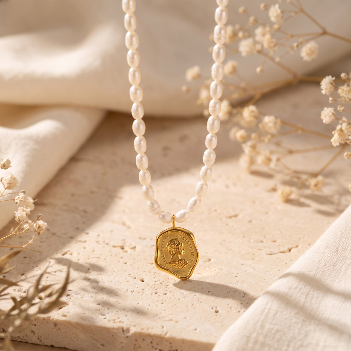 Necklace of white pearl-inspired beads suspended over a beige stone surface with a gold-tone coin pendant.