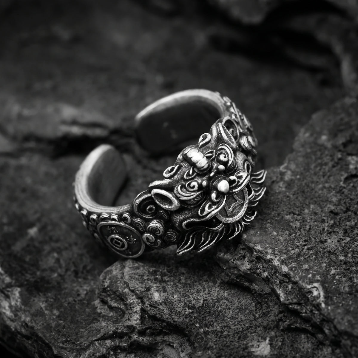 Angled view of the oxidized silver Pixiu ring on dark rock, showing the open band and side detailing.