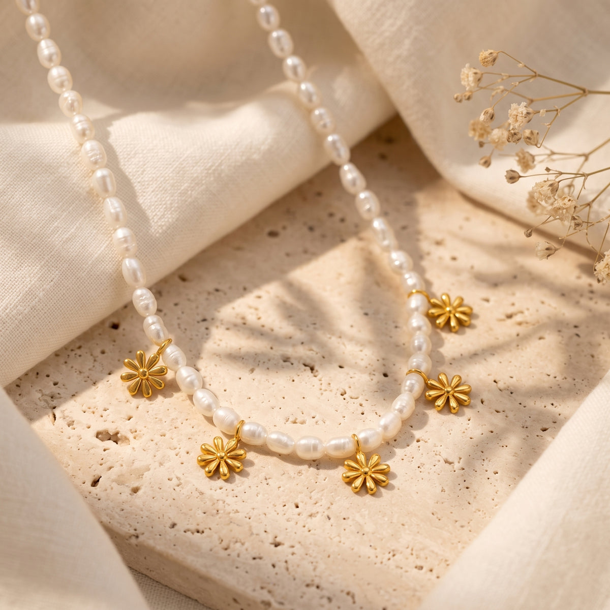 Flat lay of a white pearl bead necklace with five gold-tone daisy charms on a porous stone surface.