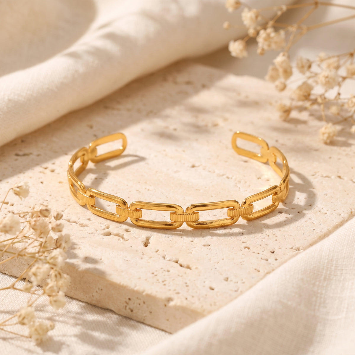 Gold-tone open-cuff paperclip link bracelet arranged horizontally on a porous stone slab.