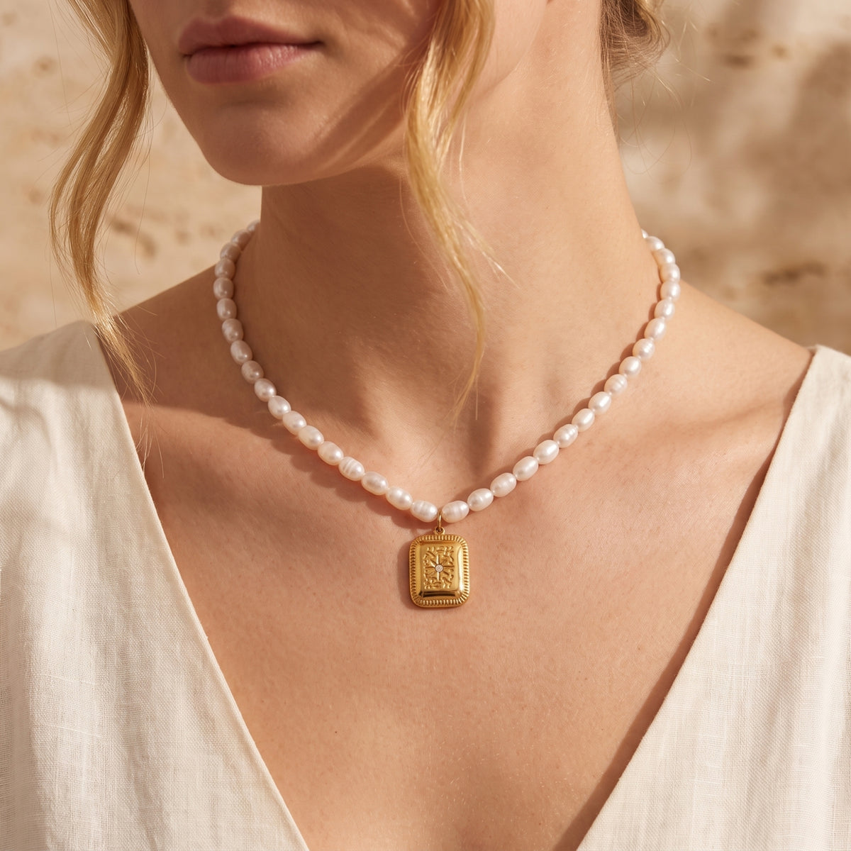 Front view of a model wearing a freshwater pearl necklace with a rectangular gold-tone starburst pendant.