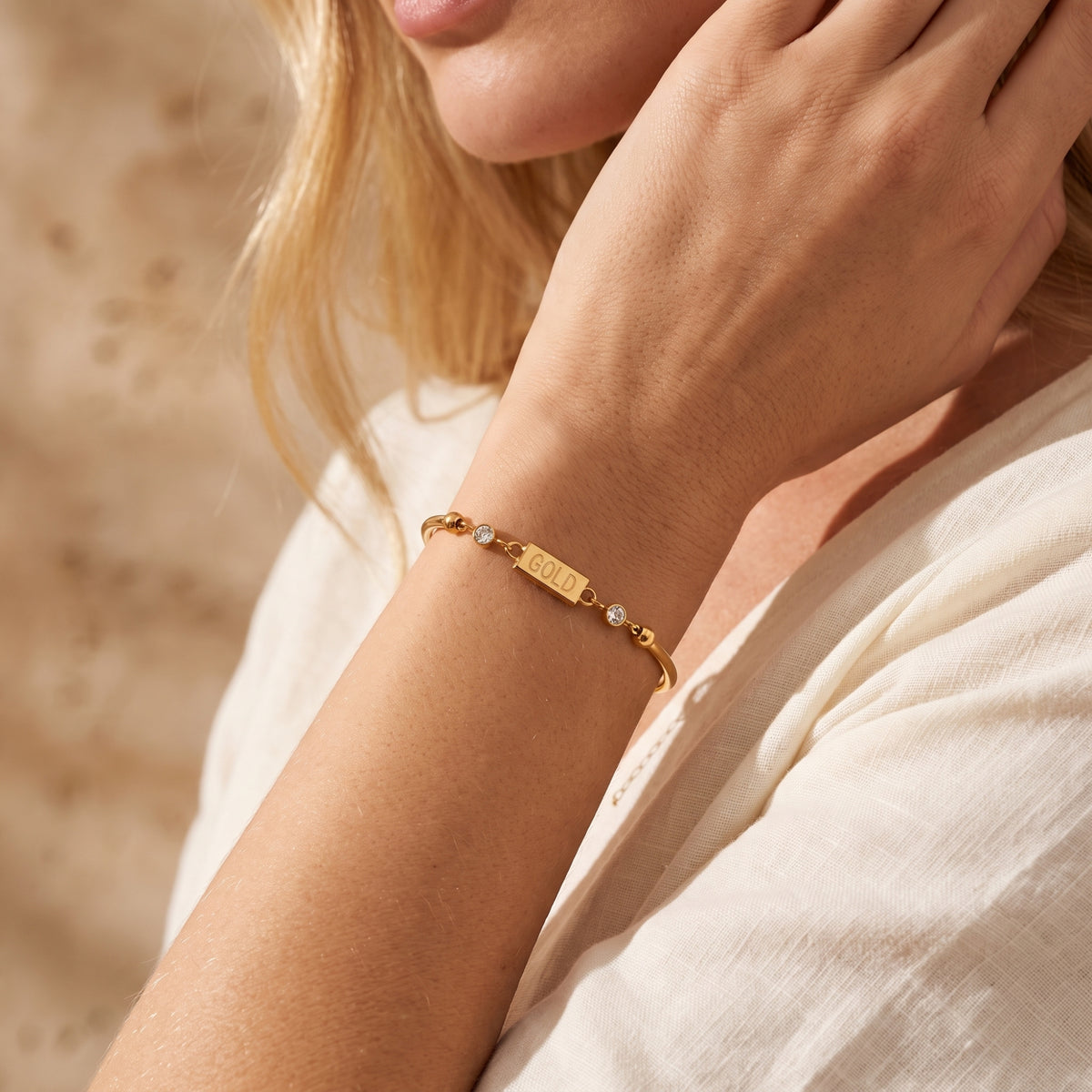 Close-up of a model wearing the gold-tone bar station bracelet on her wrist near her face.