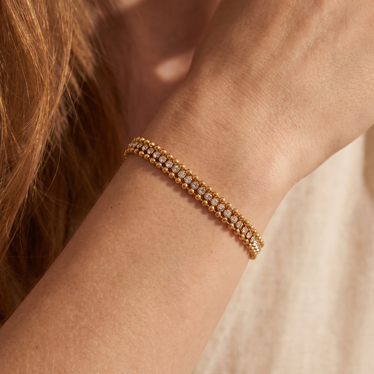Close-up of a gold-tone triple-row beaded bracelet with cubic zirconia worn on a wrist.