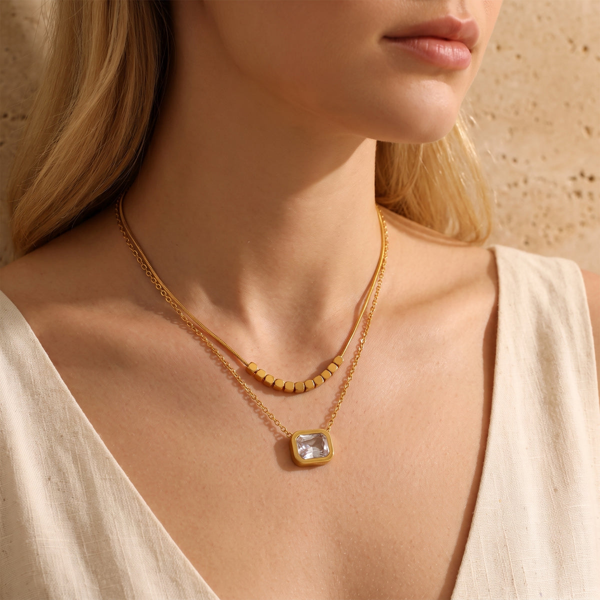 Wider view of a model wearing a gold-tone layered necklace with cube accents and a square clear pendant.
