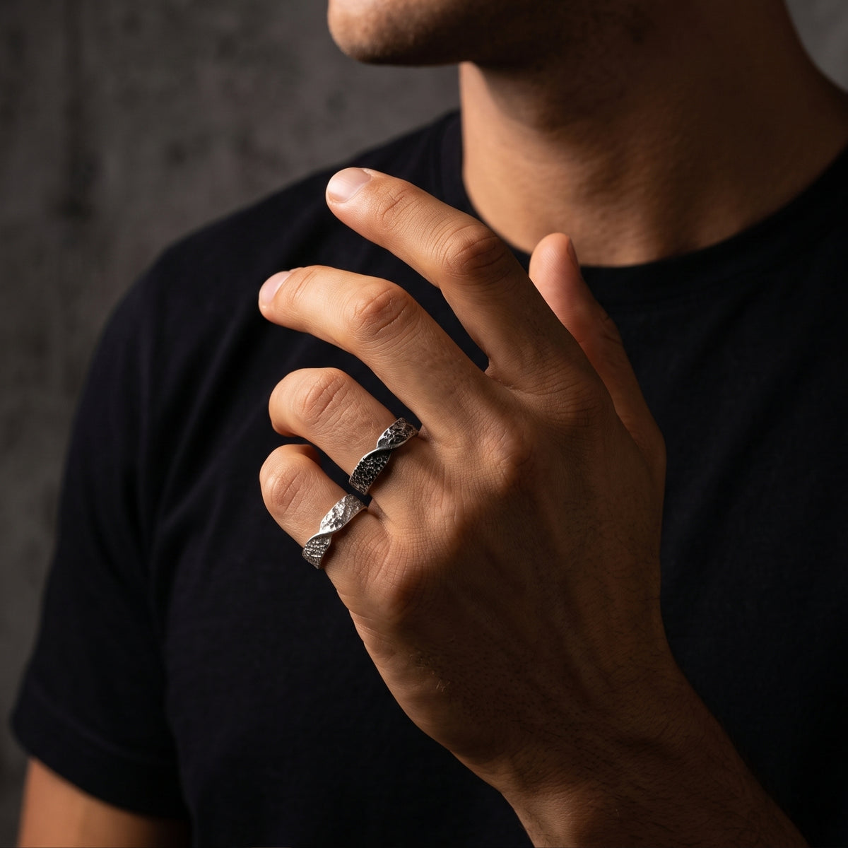 Man wearing silver and dark oxidized hammered twist bands on his hand against a dark shirt.