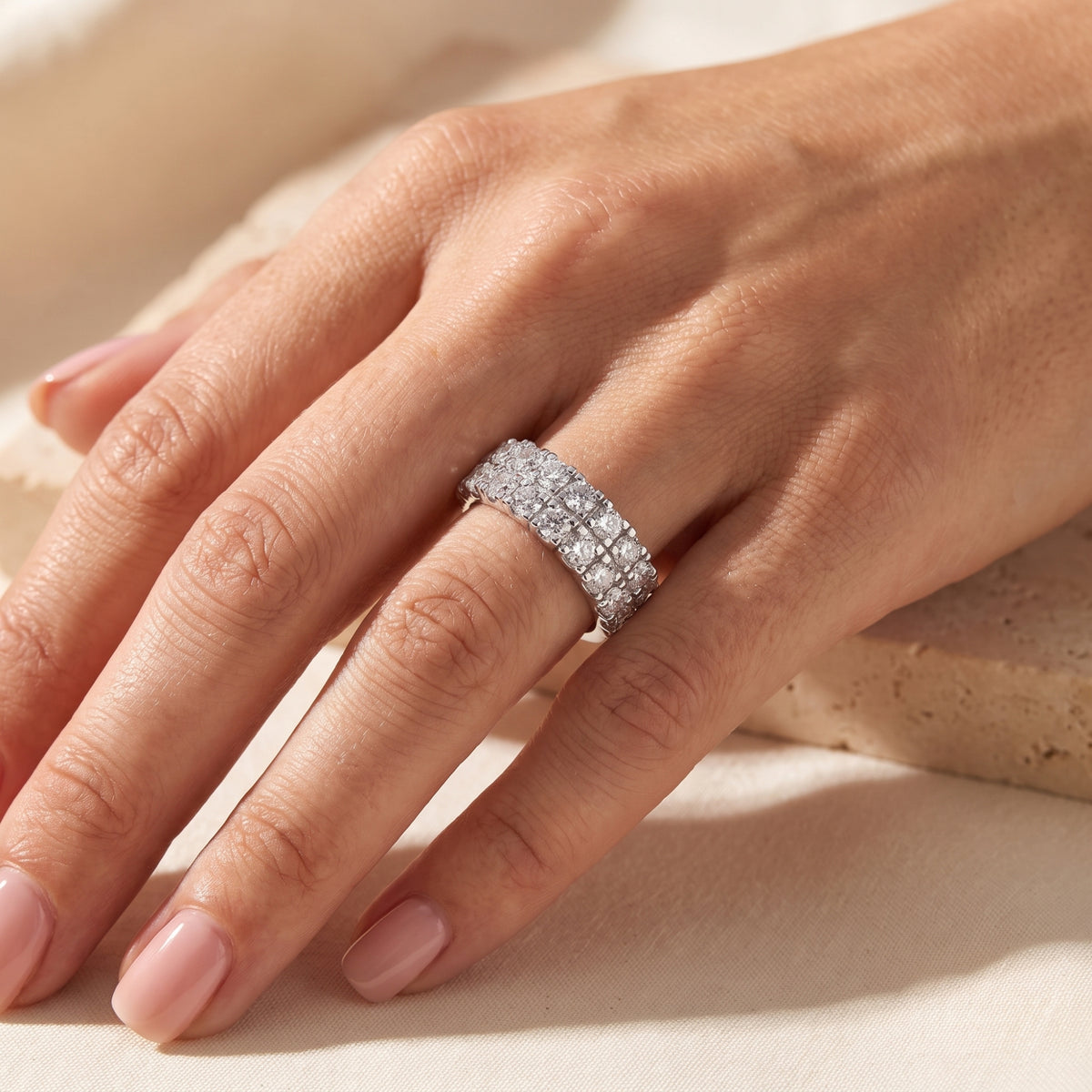 Hand wearing a silver double-row clear-stone band ring, resting on a cream-colored surface.