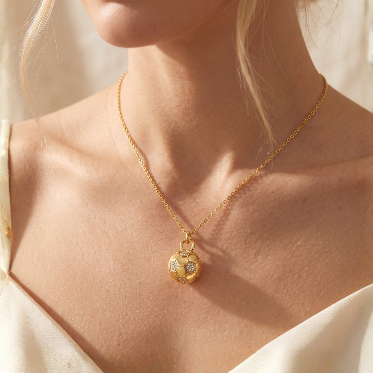 Frontal view of a model wearing a gold-tone soccer ball pendant necklace with simulated-diamond accents.
