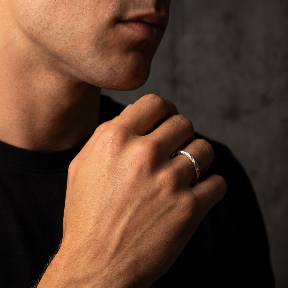 Close-up of a man's raised hand beside his face, wearing the textured open ring on his ring finger.