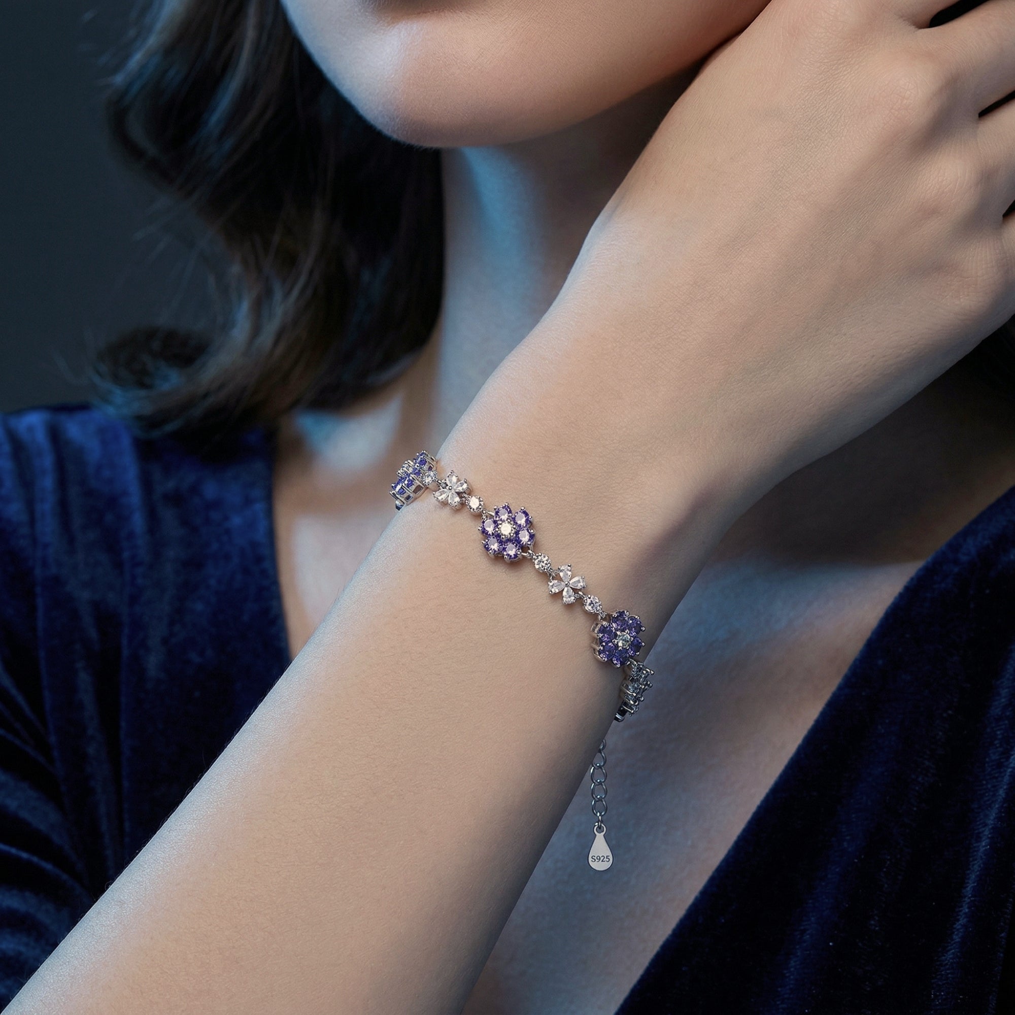 Tanzanite cluster bracelet in sterling silver showcased on a model's wrist against a dark blue background.