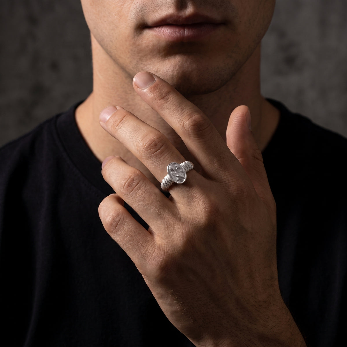 Model posing with a hand near the chin, wearing the silver tulip signet ring on a raised middle finger.