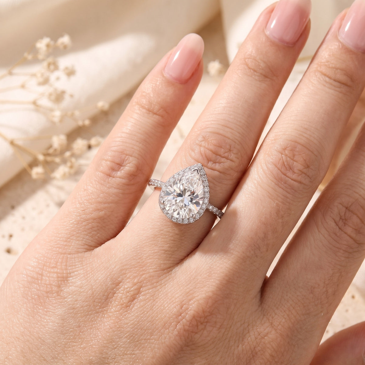 Close-up of a hand wearing a silver pear-cut halo ring with a pavé band.